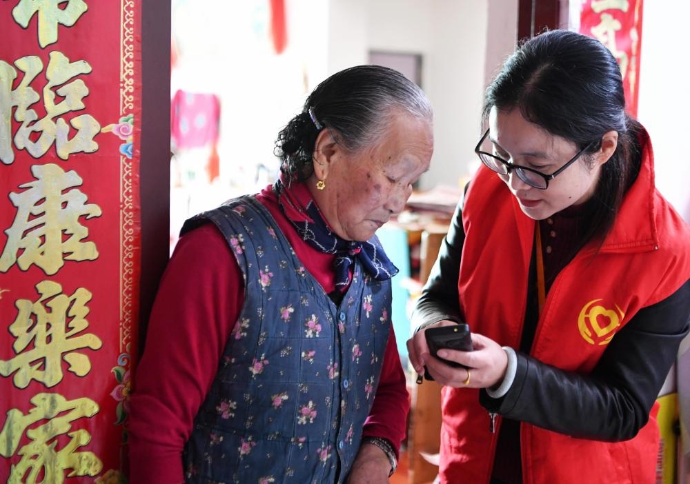 在福州市長(zhǎng)樂(lè)區(qū)航城街道籌岐村，智慧養(yǎng)老平臺(tái)派駐社區(qū)的助老員（右）在為老人陳鳳英（左）講解養(yǎng)老定制手機(jī)的用法（2021年11月26日攝）。新華社記者 魏培全 攝