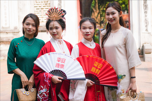 身穿古裝的中國游客和身穿越南傳統(tǒng)服飾奧黛的越南青年在文廟門前合影。