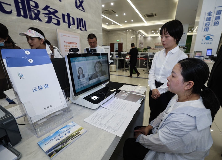 在浙江省嘉興市秀洲區(qū)王江涇鎮(zhèn)便民服務(wù)中心的“跨域通辦·云綜窗”窗口，辦理開業(yè)登記的個(gè)體工商戶（右一）通過該系統(tǒng)與江蘇省蘇州市吳江區(qū)盛澤鎮(zhèn)行政審批局工作人員視頻連線，進(jìn)行身份讀取及材料線上審核（2024年5月9日攝）。新華社記者 徐昱 攝